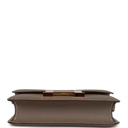 Taupe leather bag underside with center hardware bar and stitched edges