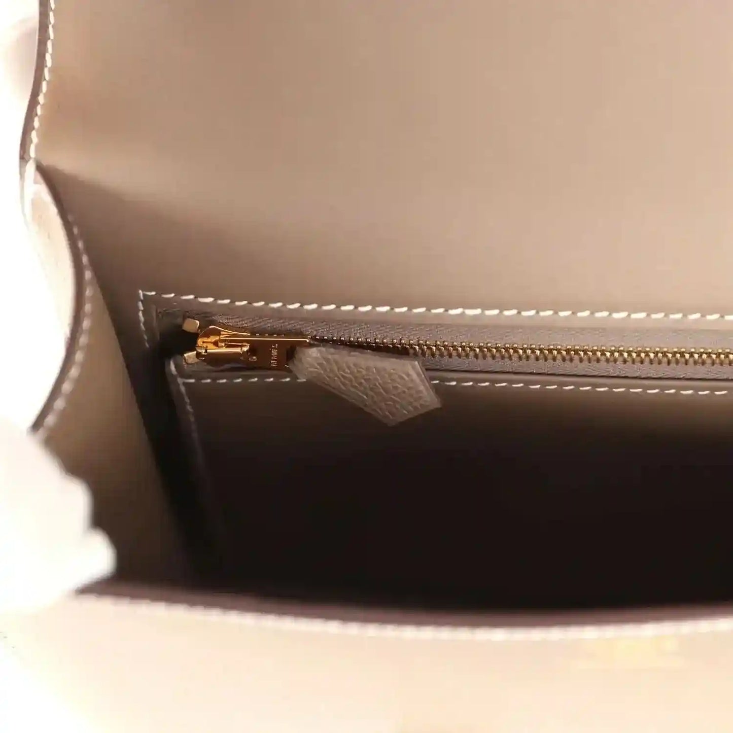 Taupe leather interior with gold-tone zipper pull and stitched pocket edge