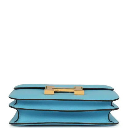 Mini crossbody bag in light blue leather shown from underside with gold hardware bar