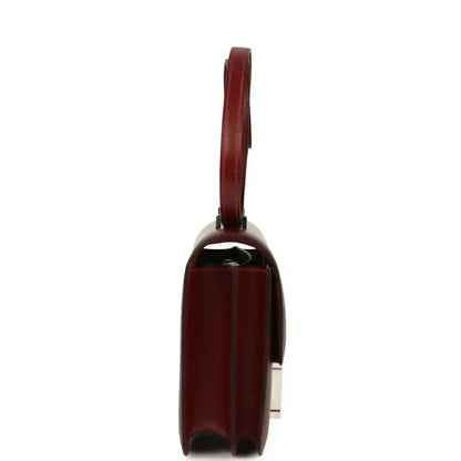 Burgundy leather bag side profile with structured edges and metal hardware.