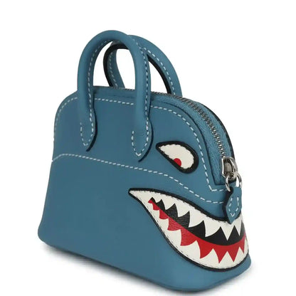 Hermes shark bag charm in blue leather, angled view with shark appliqué and front zipper