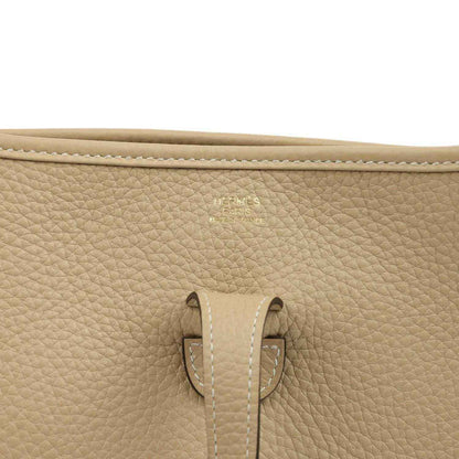 Tan textured leather bag close-up showing cream stitching and strap attachment detail