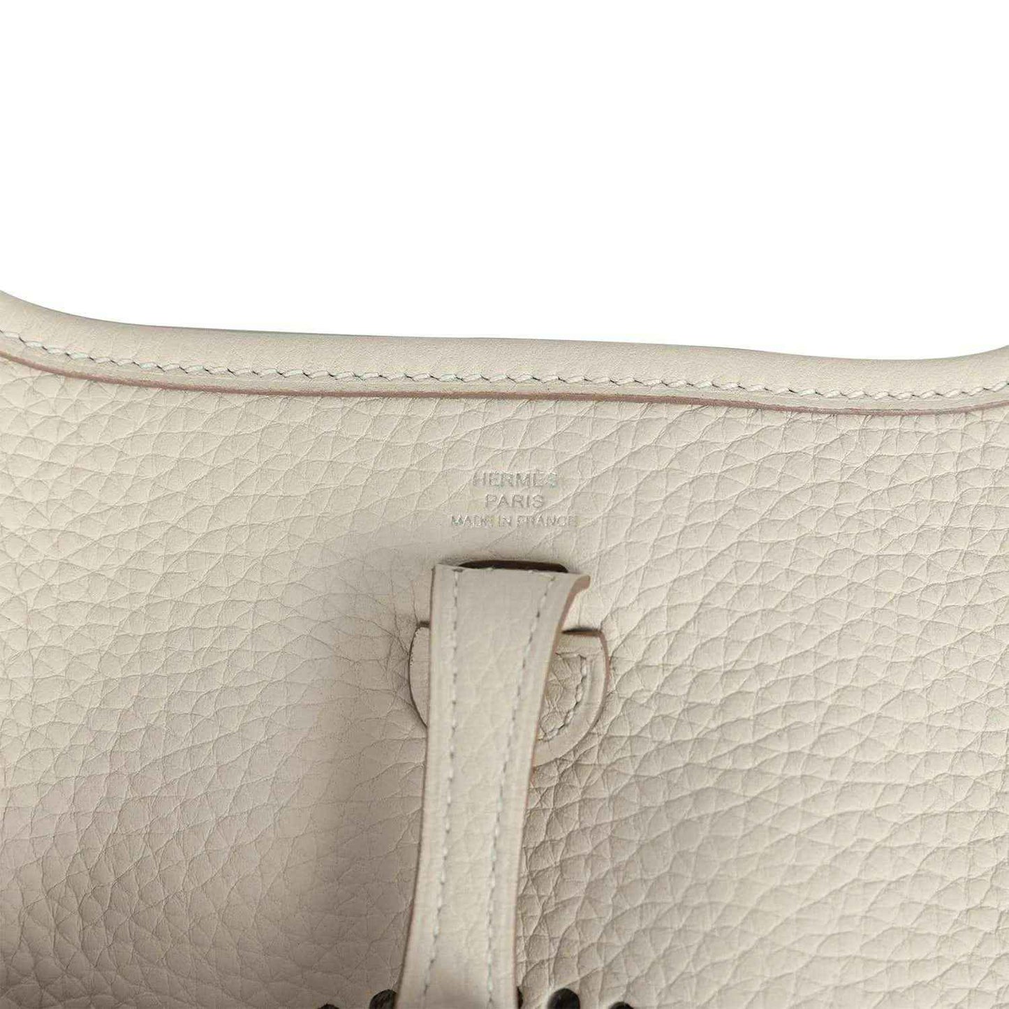Light cream leather bag close-up of strap attachment and embossed logo stamp