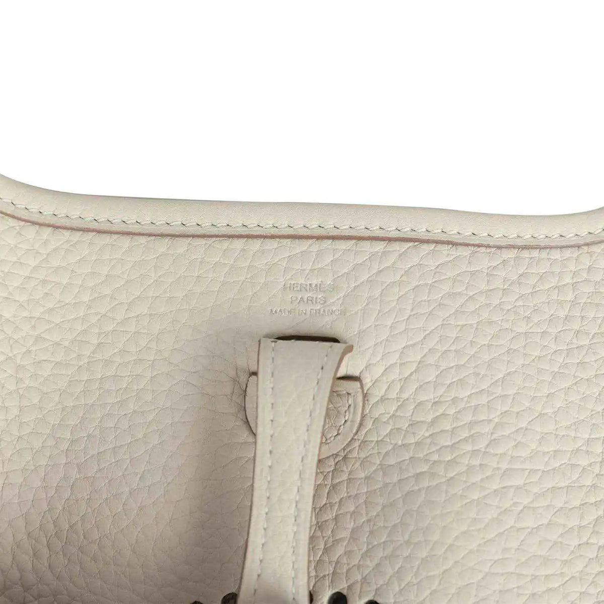Light cream leather bag close-up of strap attachment and embossed logo stamp