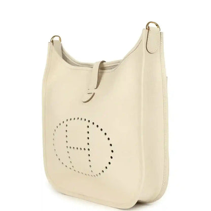 Cream leather shoulder bag with perforated logo on front panel and top strap with gold-tone hooks.
