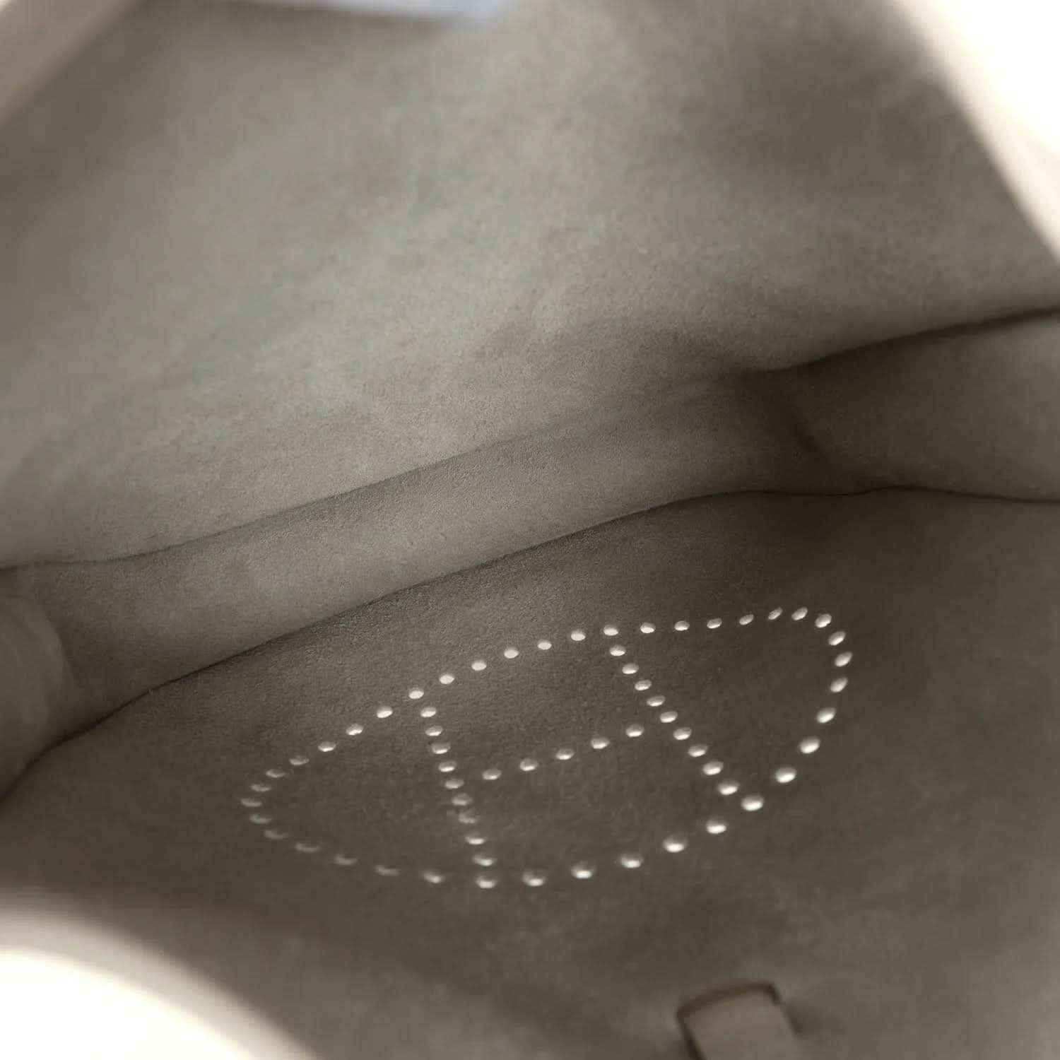 Gray interior lining of a cream leather bag with perforated “E” logo and stitching.