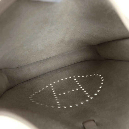 Gray interior lining of a cream leather bag with perforated “E” logo and stitching.