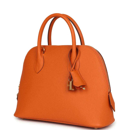 Orange leather handbag angled front with gold padlock clasp, dual handles, and side tab detail.