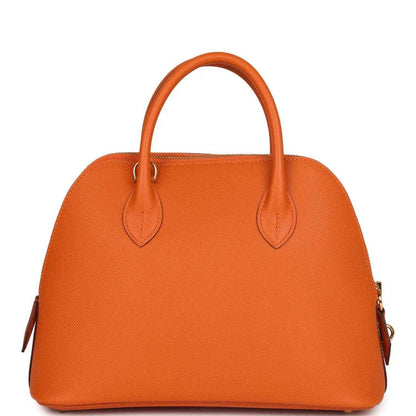 Orange leather handbag front view with dual top handles and decorative strap detail, gold hardware.