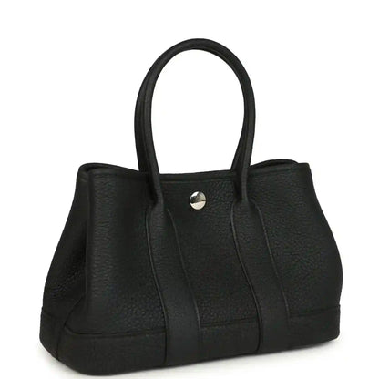 Black leather tote bag with top handles, side panels, and snap button