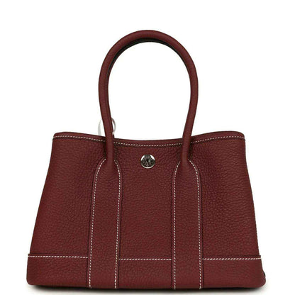 Red leather tote bag with top handles, front snap button and stitched panels.
