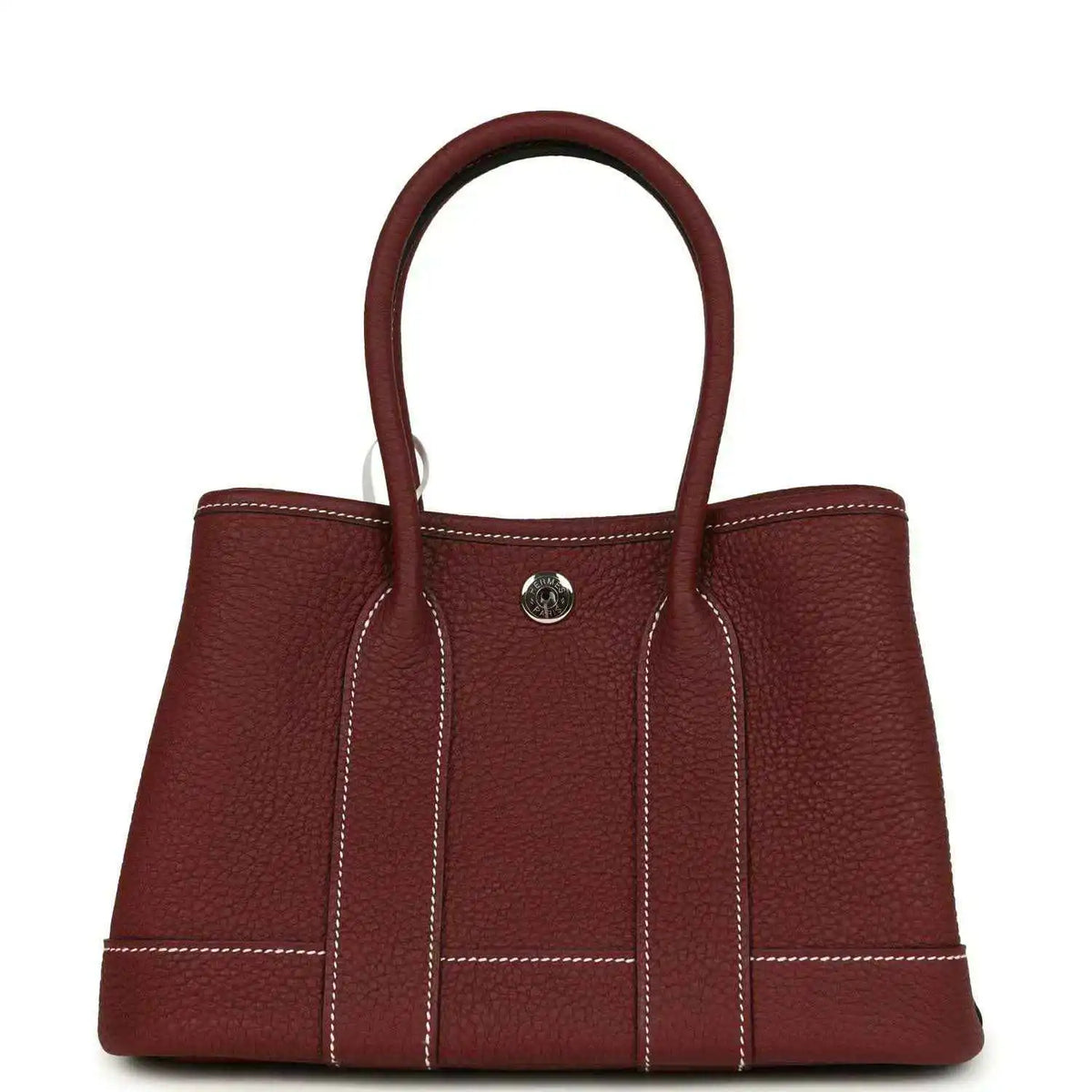 Red leather tote bag with top handles, front snap button and stitched panels.