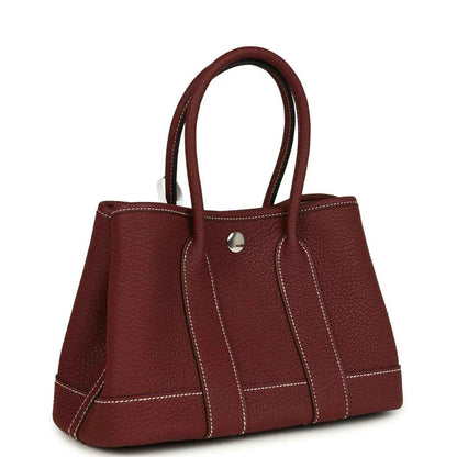 Red leather tote bag with top handles and stitched front panels, angled side view.