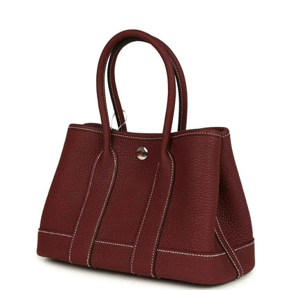 Red leather tote bag with top handles and stitched trim across the sides.