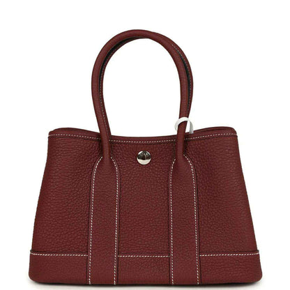 Red leather tote bag with top handles, front snap button, and stitched front panels.