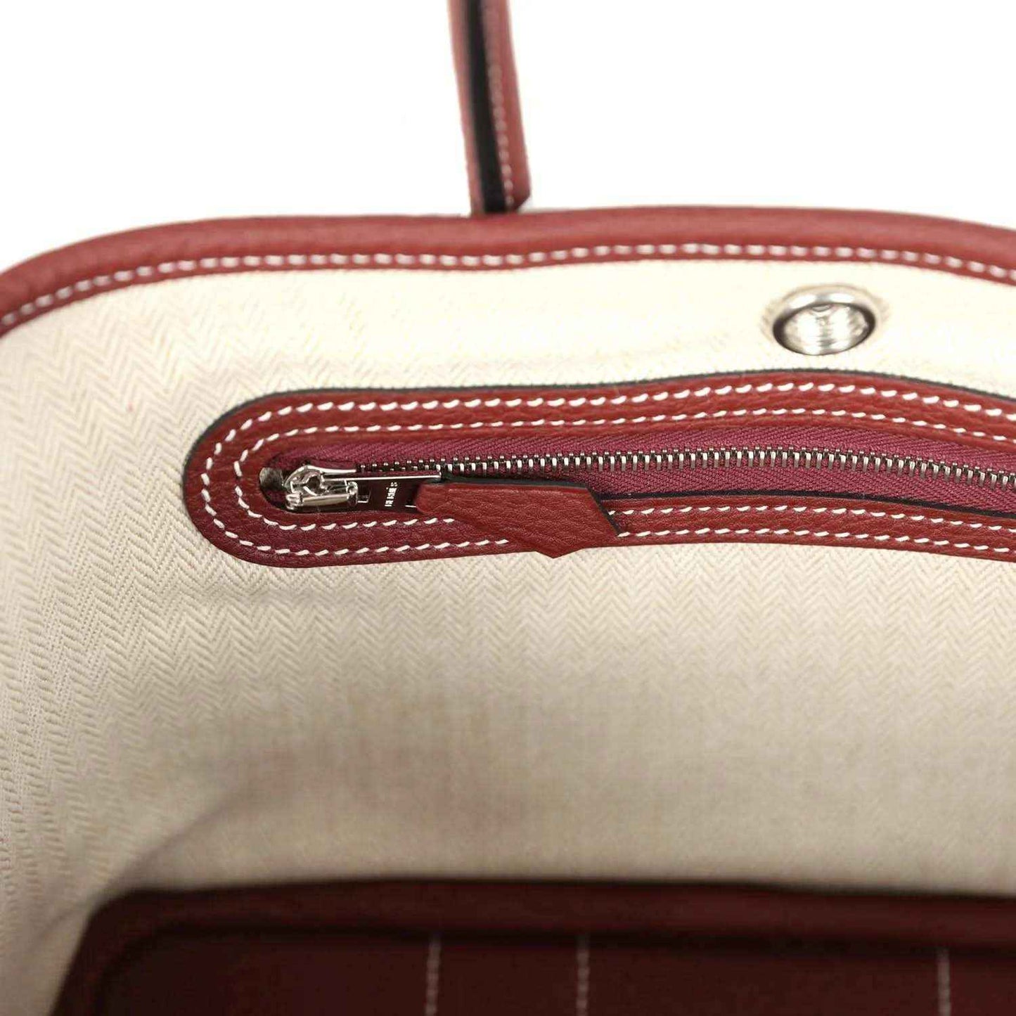 Canvas-lined tote zip pocket with burgundy leather trim and metal zipper pull.