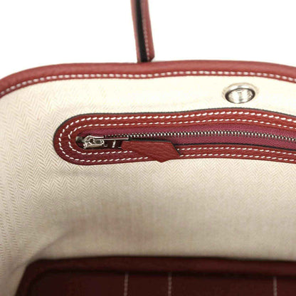 Canvas-lined tote zip pocket with burgundy leather trim and metal zipper pull.