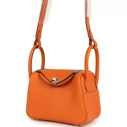 Orange clemence mini handbag with short handles, crescent flap, and metal clasp hardware.