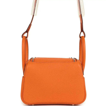 Orange structured leather mini shoulder bag with flap top and top carry handles.