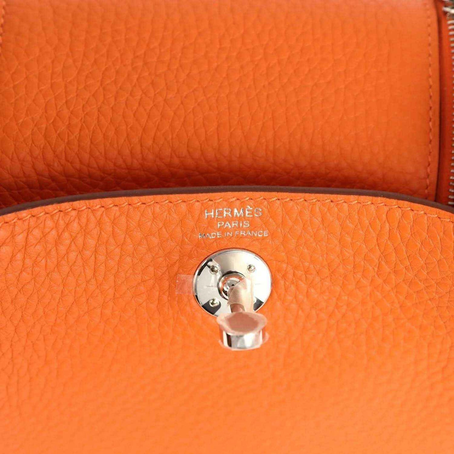 Orange pebble-grain leather handbag detail with round engraved pull-tab and metal clasp.