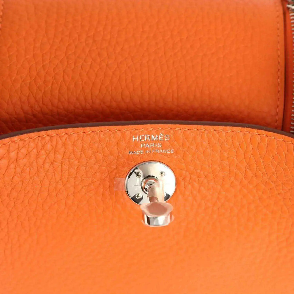 Orange pebble-grain leather handbag detail with round engraved pull-tab and metal clasp.