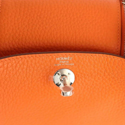 Orange pebble-grain leather handbag detail with round engraved pull-tab and metal clasp.