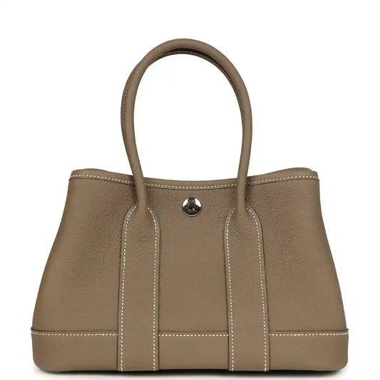 Taupe leather mini tote bag with two top handles and front snap pocket, stitched panels