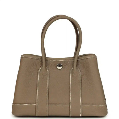 Taupe leather mini tote bag with top handles and front snap button, vertical stitched strips