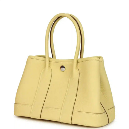 Yellow leather tote bag with curved top handles and front snap button, seam detailing