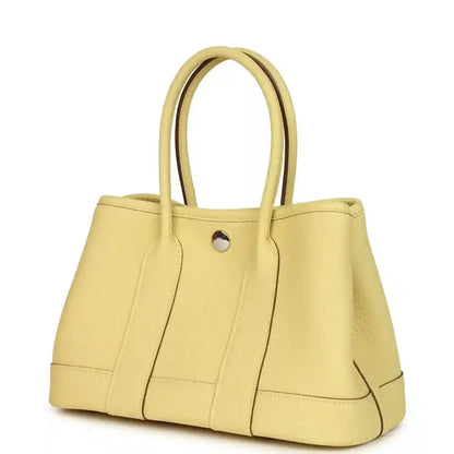 Yellow leather tote bag with curved top handles and front snap button, seam detailing