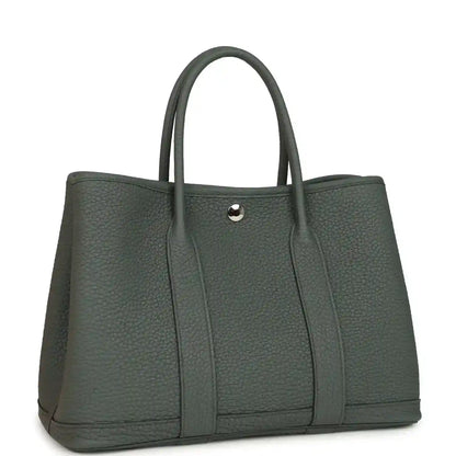 Leather tote bag with top handles and snap front tab, textured dark green exterior