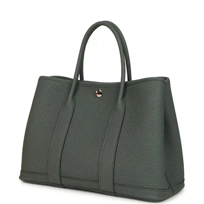 Leather tote bag with top handles and snap front tab, angled view, textured dark green
