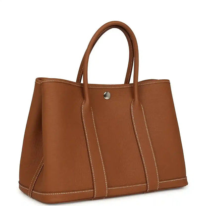 Brown leather tote bag with two handles and central gold-tone snap closure