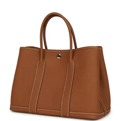 Brown leather tote bag with structured sides, two handles, and gold-tone snap
