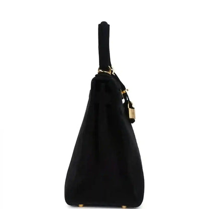 Black suede top-handle handbag standing silhouette with gold strap hardware