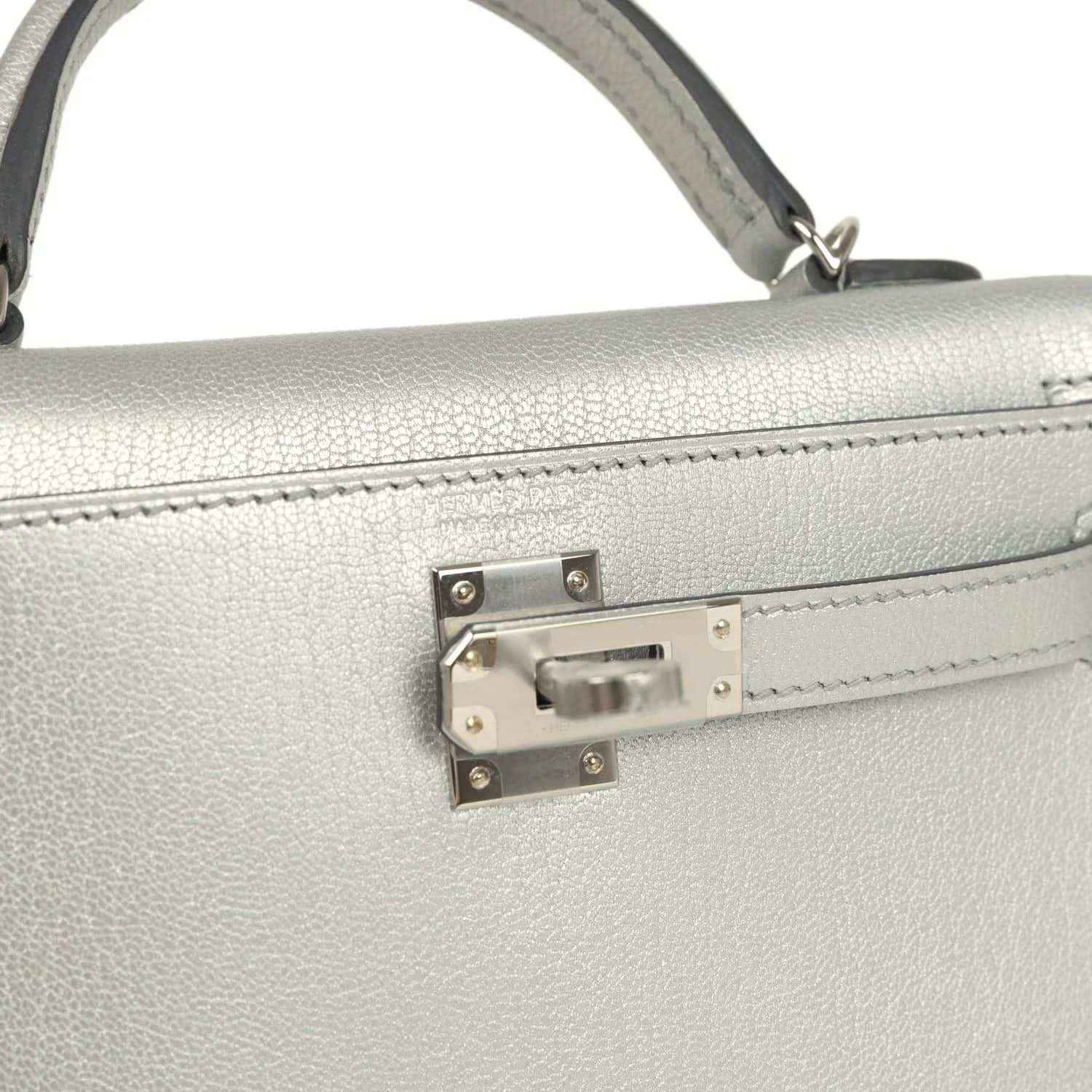 Front turn-lock hardware on light gray mini handbag with top handle strap