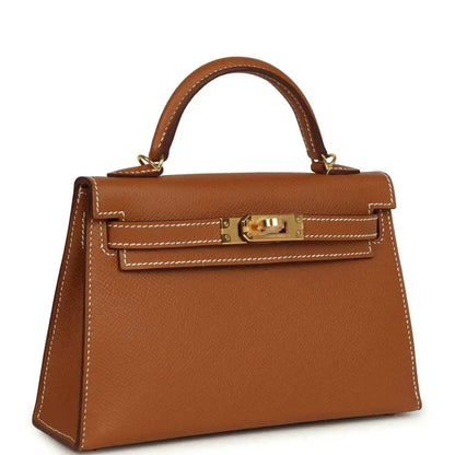 Mini leather handbag with top handle and gold front clasp, tan textured finish