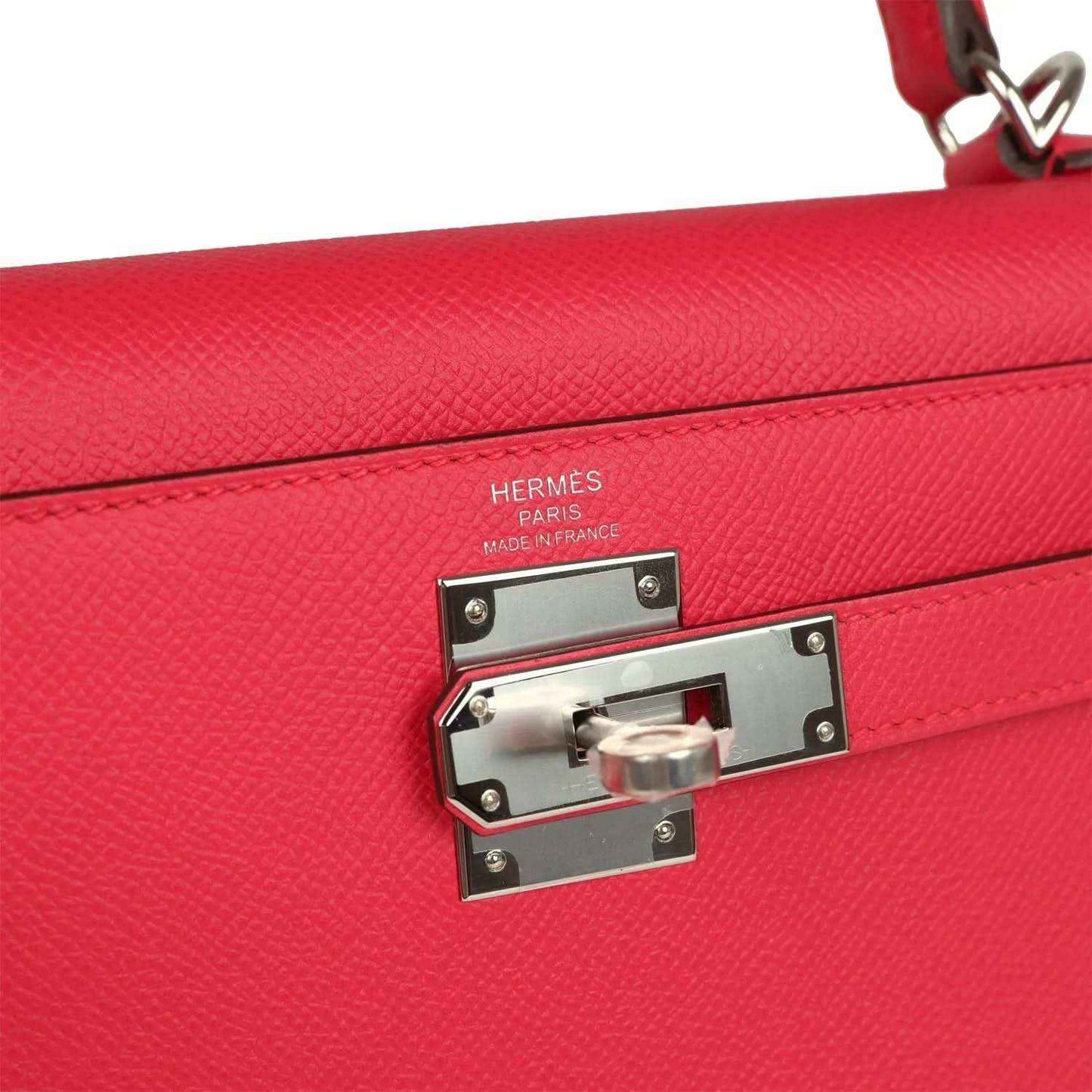 Hermes hardware lock plate on red leather handbag flap with engraved branding.