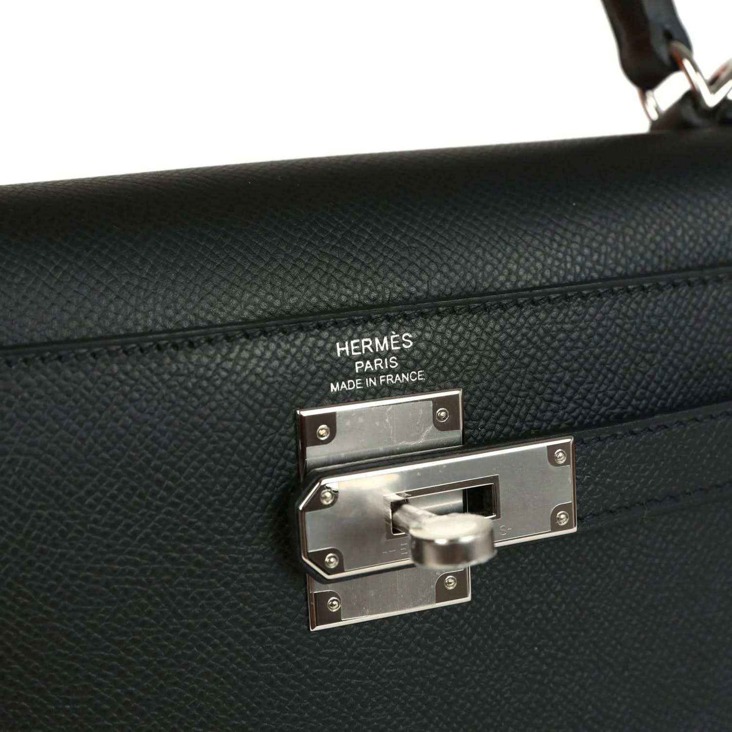 Metal turn-lock closure on a textured leather handbag front with engraved plate