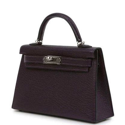 Purple leather handbag with top handle, front flap and metal clasp hardware.