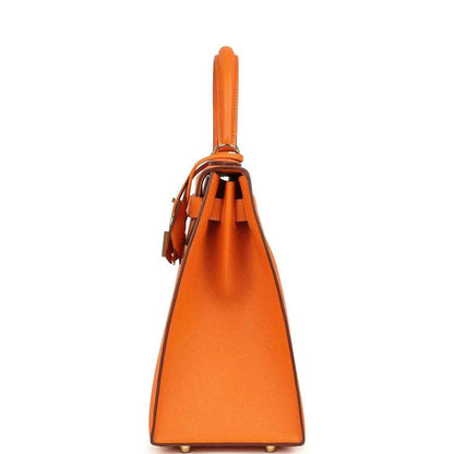 Orange Epsom leather Kelly handbag side view with top handle and strap tabs