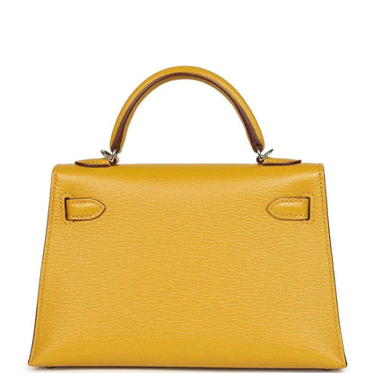 Yellow leather handbag front with curved top handles and symmetrical flap locks, silver-tone hardware