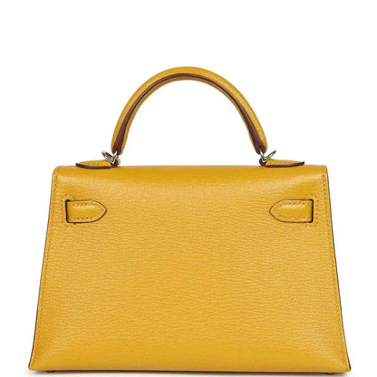 Yellow leather handbag front with curved top handles and symmetrical flap locks, silver-tone hardware