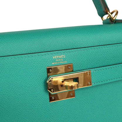 Hermes logo turn-lock on green leather Kelly-style bag with gold hardware plate.