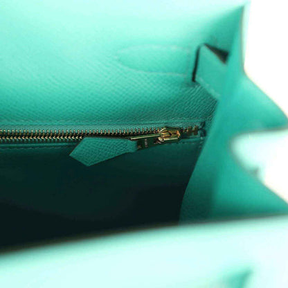 Green leather handbag interior with gold zipper and small fabric tab near pocket edge.