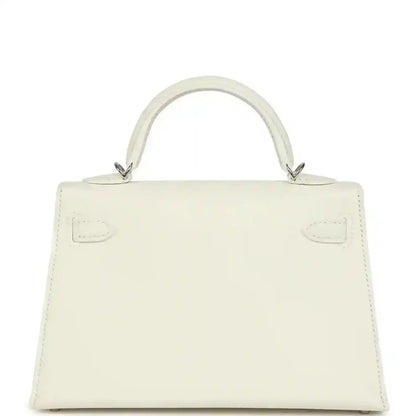 White mini Kelly-style handbag back view with top handles and stitched panel details