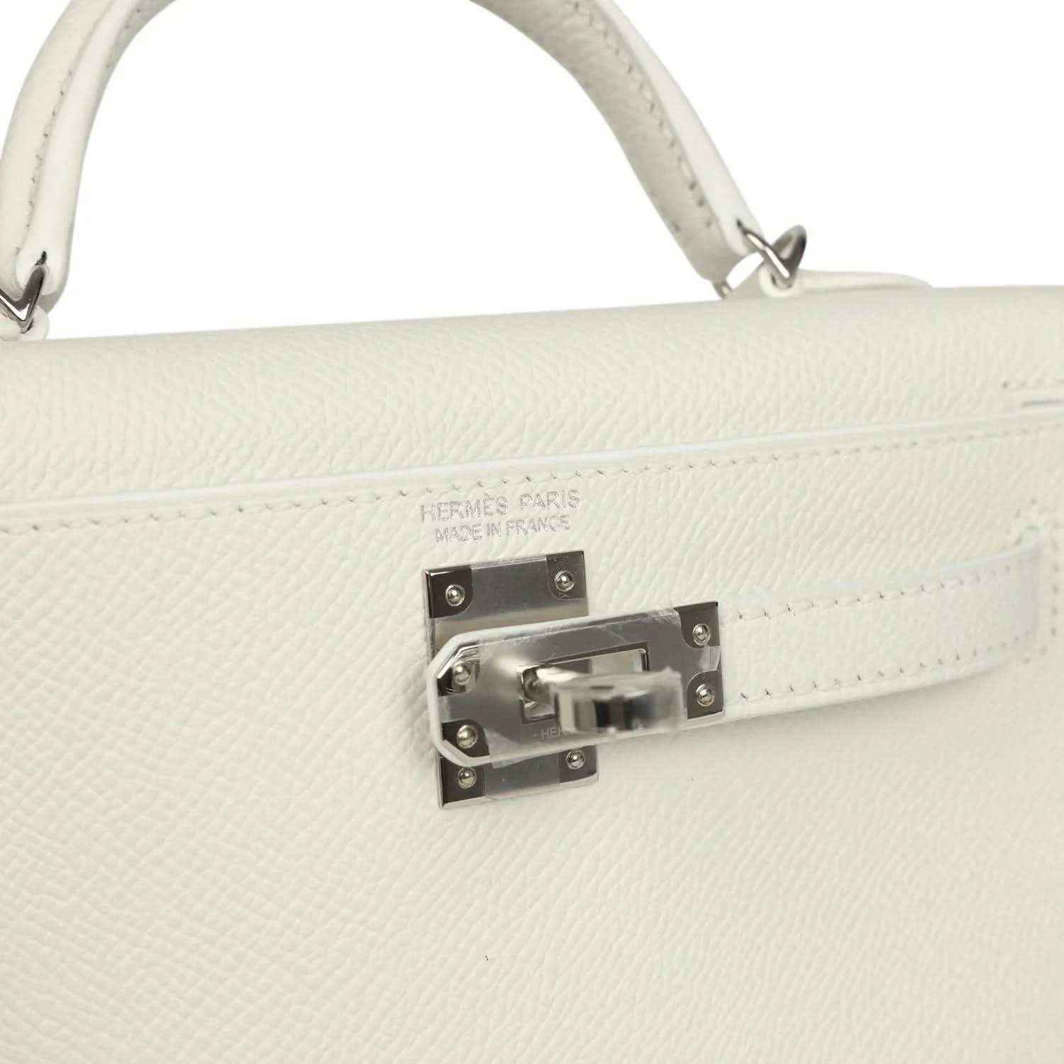 White mini Kelly-style handbag close-up of front clasp hardware on the flap