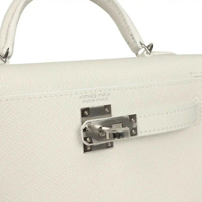 White mini Kelly-style handbag close-up of front clasp hardware on the flap