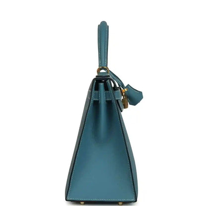 Blue leather handbag with upright silhouette, top handle, and attached leather strap loop.