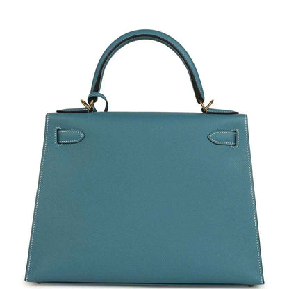 Blue leather handbag with two side gussets, stitched flap, and top handles with gold-tone rings.